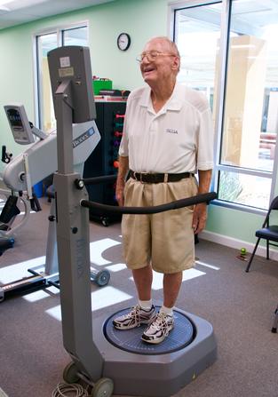 Older man performing standing balance training on a Biodex machine in the clinic gym