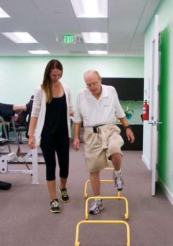 Physical therapist assisting an older man with a hurdle step-over balance exercise